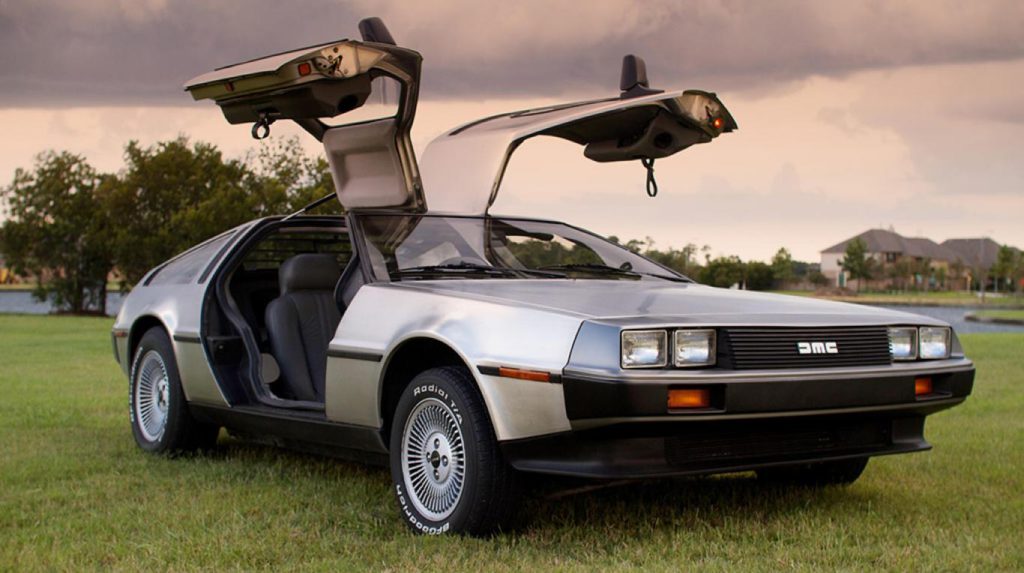 Imagen del DeLorean de la película Regreso al Futuro con las puertas abiertas. El coche está en la explanada de un campo.